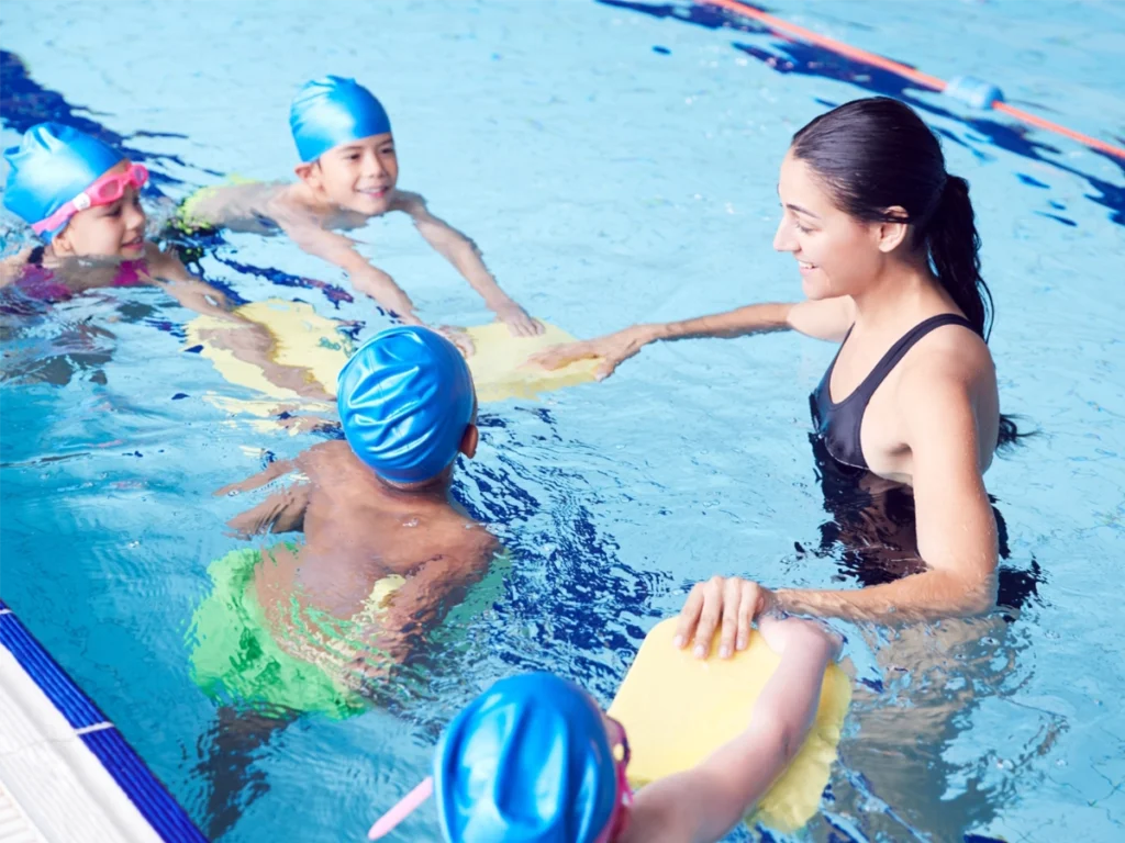 A swim teacher helps students learn to kick with the help of body boards