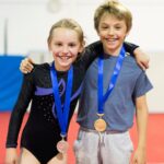 Two young gymnasts smile while wearing their medals