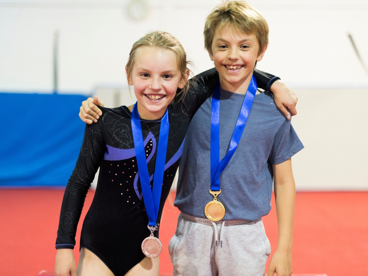 Two young gymnasts smile while wearing their medals